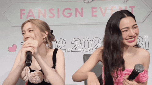two women laughing in front of a sign that says fansign event on it