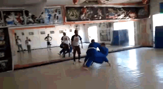 a group of people are practicing martial arts in a gym while a referee watches .
