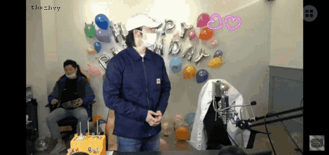 a man wearing a mask stands in front of balloons that say happy day