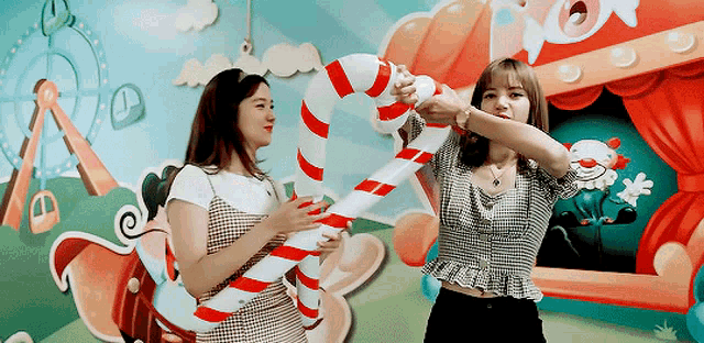 two girls are holding a large candy cane in front of a clown