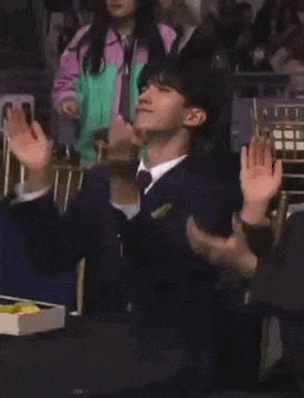 a man in a suit and tie is sitting in a chair and clapping his hands .