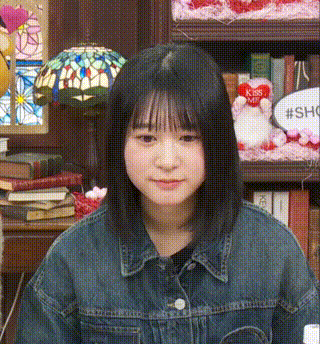 a girl in a denim jacket is sitting in front of a bookshelf with a lamp .
