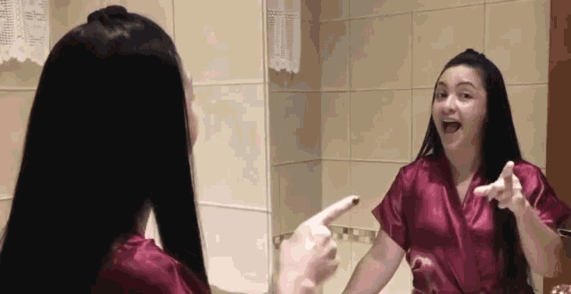 a woman is pointing at herself in the mirror while wearing a purple robe .