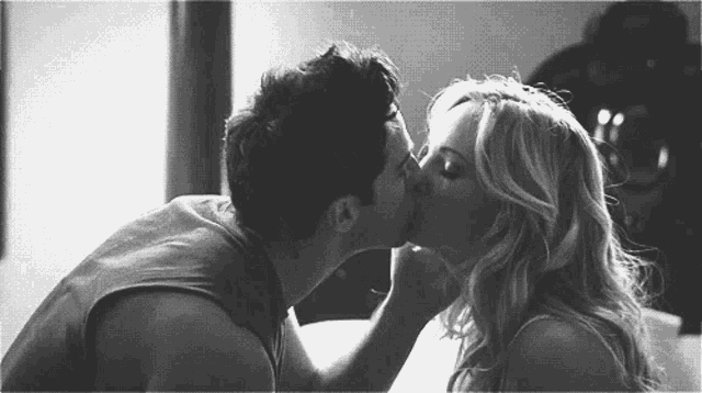 a black and white photo of a man and woman kissing .