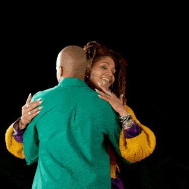 a man in a green shirt and a woman in a yellow sweater are hugging each other