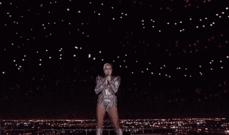 a woman in a silver outfit is dancing on a stage in front of a starry sky .