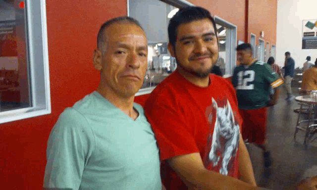 a man in a red shirt with the number 12 on it stands next to another man in a green shirt