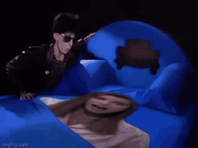 a woman is smiling while laying on a bed with blue pillows .