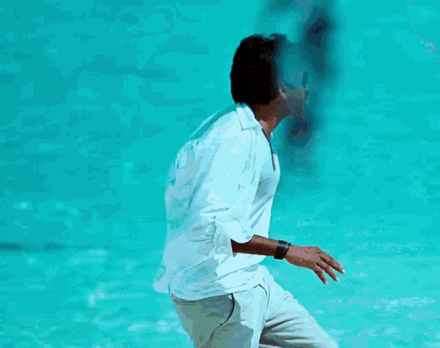 a man wearing sunglasses and a white shirt stands in front of a blue water surface