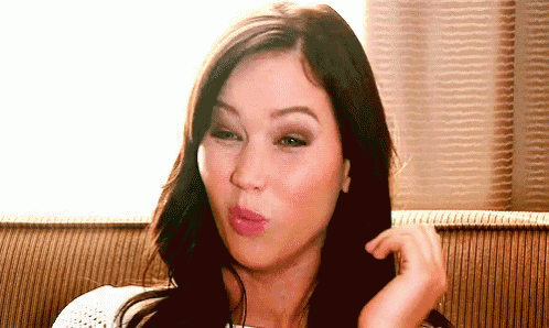 a woman is sitting on a couch with her hand in her hair and making a funny face .