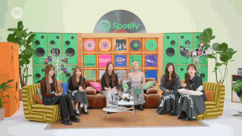 a group of women are sitting in front of a wall that says spotify