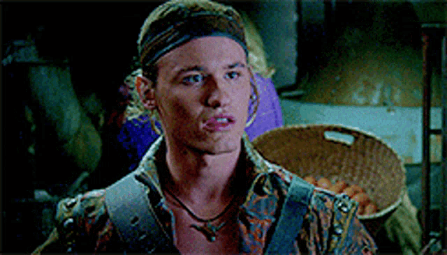 a man wearing a headband and a necklace is standing in a dark room