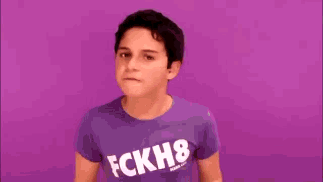 a young boy wearing a purple t-shirt with the word fckh8 on it is pointing his finger at the camera .