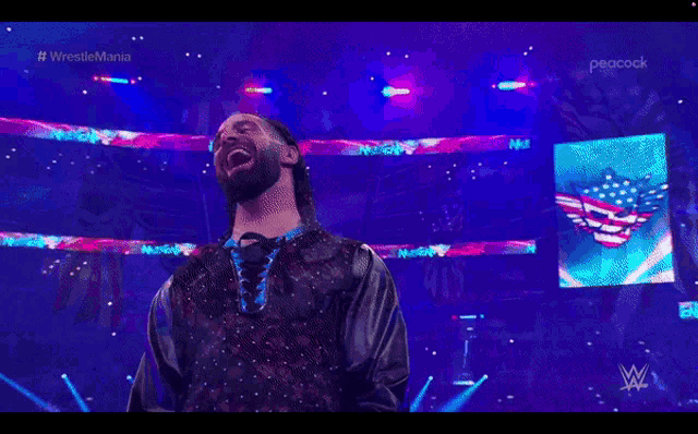 a wrestler is laughing on a stage while wearing a black and blue outfit .