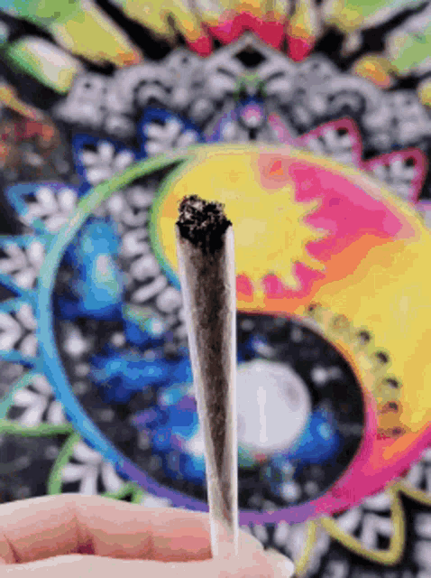 a person is holding a cigarette in front of a colorful mandala