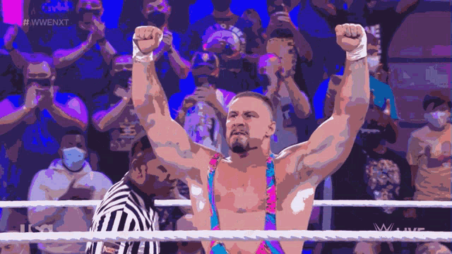 a man in a wrestling ring with his fist in the air while a referee watches