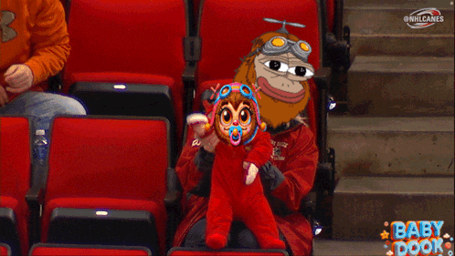 a baby in a red outfit is sitting in a stadium with a cartoon character behind it that says baby door