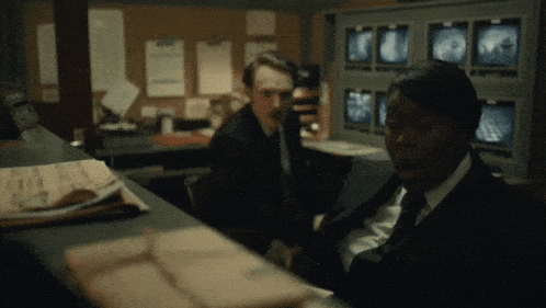 a man in a suit sits at a desk in front of a monitor