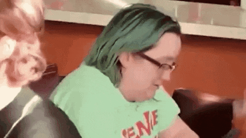 a woman with green hair and glasses is sitting on a couch eating .