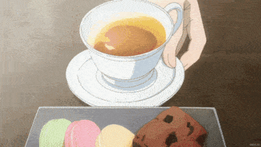 a cup of tea sits on a saucer next to a tray of macaroons