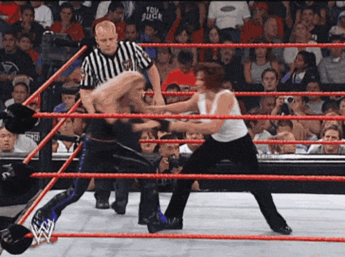 two wrestlers are fighting in a ring with a referee in the background wearing a shirt that says truly suck