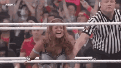 a woman is sitting in a wrestling ring with a referee in the background .