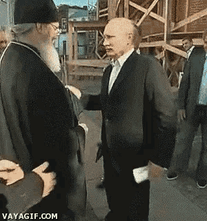 a man in a suit is shaking hands with a priest in a black hat .