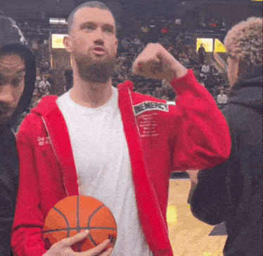 a man in a red jacket with the word mercy on it is holding a basketball