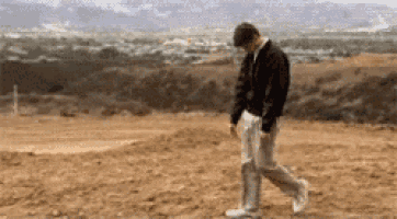 a man in a black jacket and white pants is walking through a dirt field .