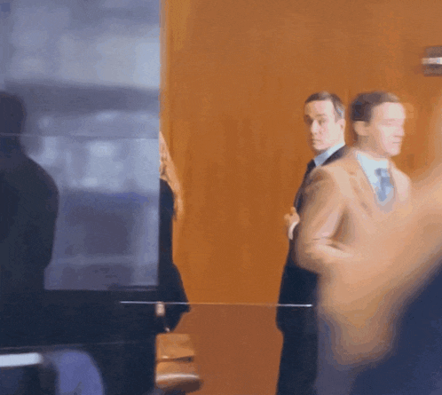 a man in a suit and tie is standing in front of a glass wall