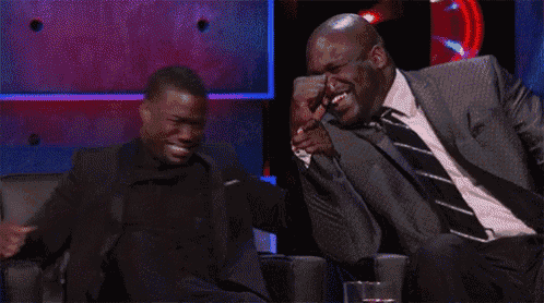 two men in suits and ties are sitting in chairs laughing .