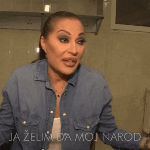 a woman in a denim shirt is standing in front of a sign that says najbolje na svetu zivi