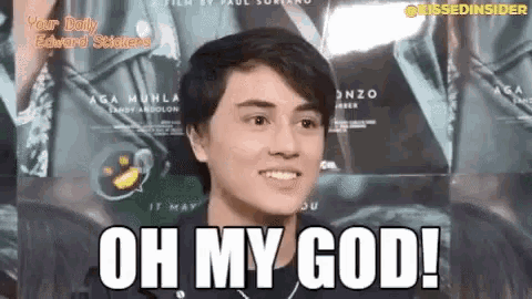 a young man is smiling and saying `` oh my god '' while standing in front of a movie poster .