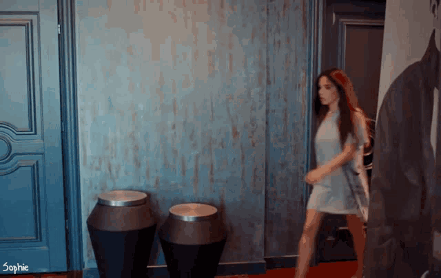 a woman in a white dress is walking in a hallway with the word sophie on the bottom right
