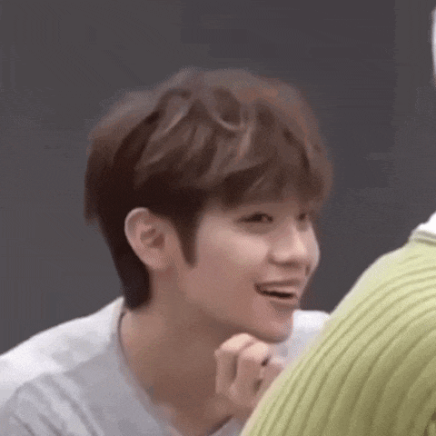 a young man with brown hair is smiling while sitting next to a green sweater .