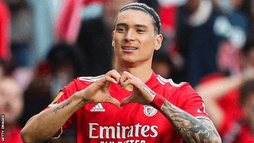 a soccer player in a red emirates jersey is making a heart shape with his hands .