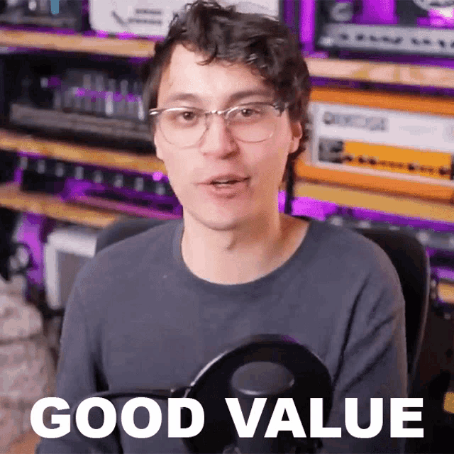 a man wearing glasses holds a microphone in front of a sign that says " good value "