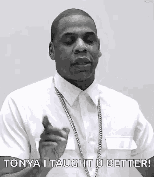 a black and white photo of a man wearing a white shirt and a gold chain pointing at the camera .
