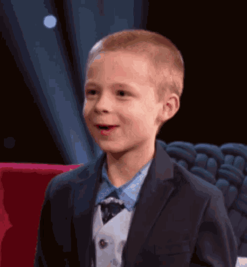 a young boy wearing a suit and tie is sitting on a chair .