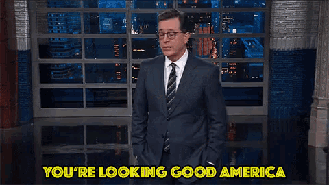 a man in a suit and tie points at the camera with the words you 're looking good america below him