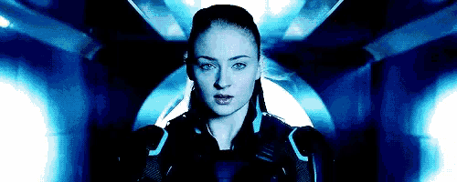 a woman is standing in a dark room with a blue light behind her and looking at the camera .