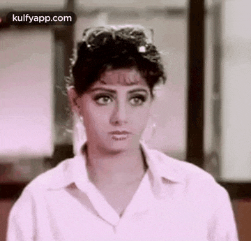 a woman in a white shirt is standing in front of a window and looking at the camera .