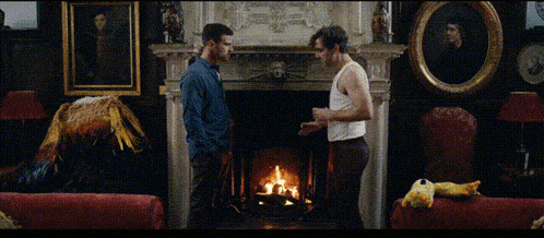 two men are standing in front of a fireplace with a bottle of beer in their hand