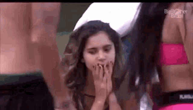 a woman is covering her mouth with her hands while standing in front of a crowd of people .