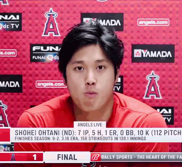a man in a red shirt stands in front of a wall with angels logos