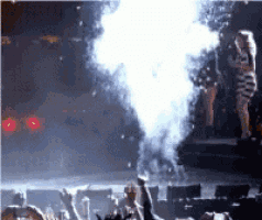 a group of people are watching a concert with smoke coming out of the stage