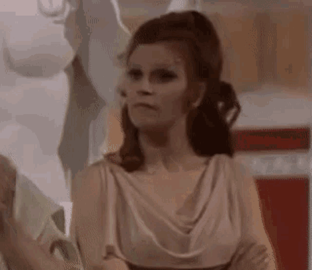a woman in a white dress is standing in front of a statue and looking at the camera .