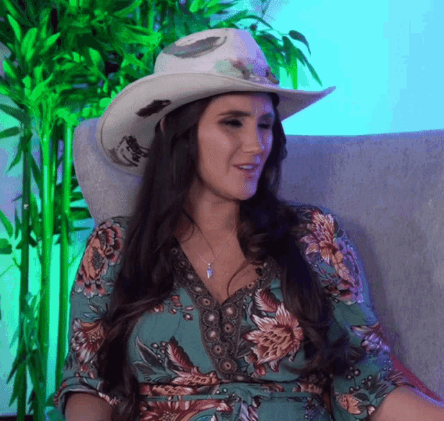 a woman wearing a cowboy hat and a floral dress is sitting in a chair
