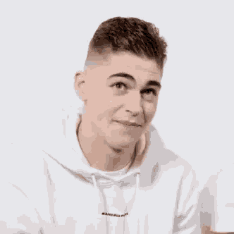 a young man wearing a white hoodie and a white shirt is looking at the camera .