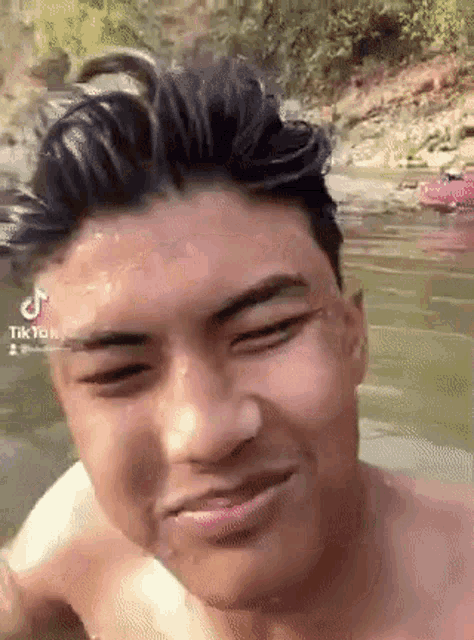 a man without a shirt is swimming in a river and smiling .